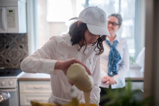 Élise pouring sourdough starter into a bowl at home in a bright kitchen and her mom looks on