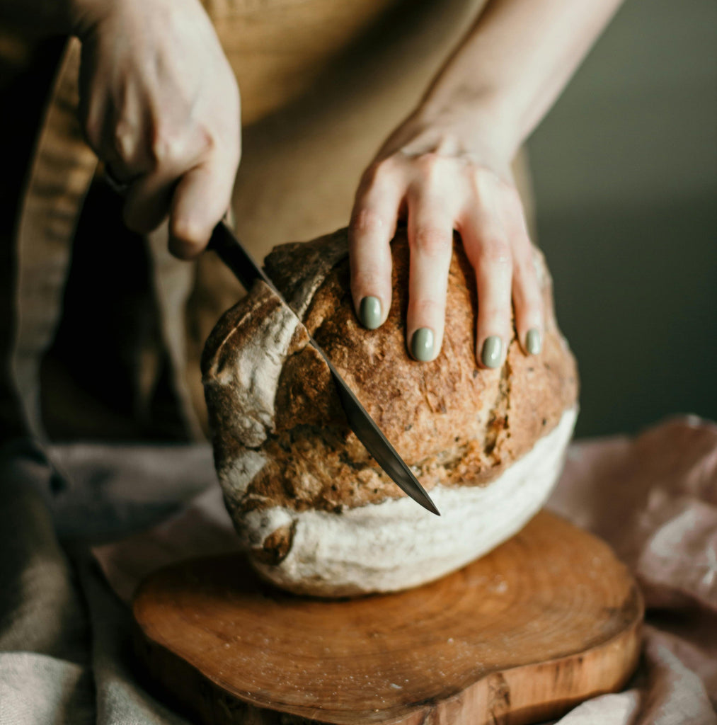 Woman slicing Freshly baked Guinness Sourdough Bread loaf with golden crust on wooden cutting board.