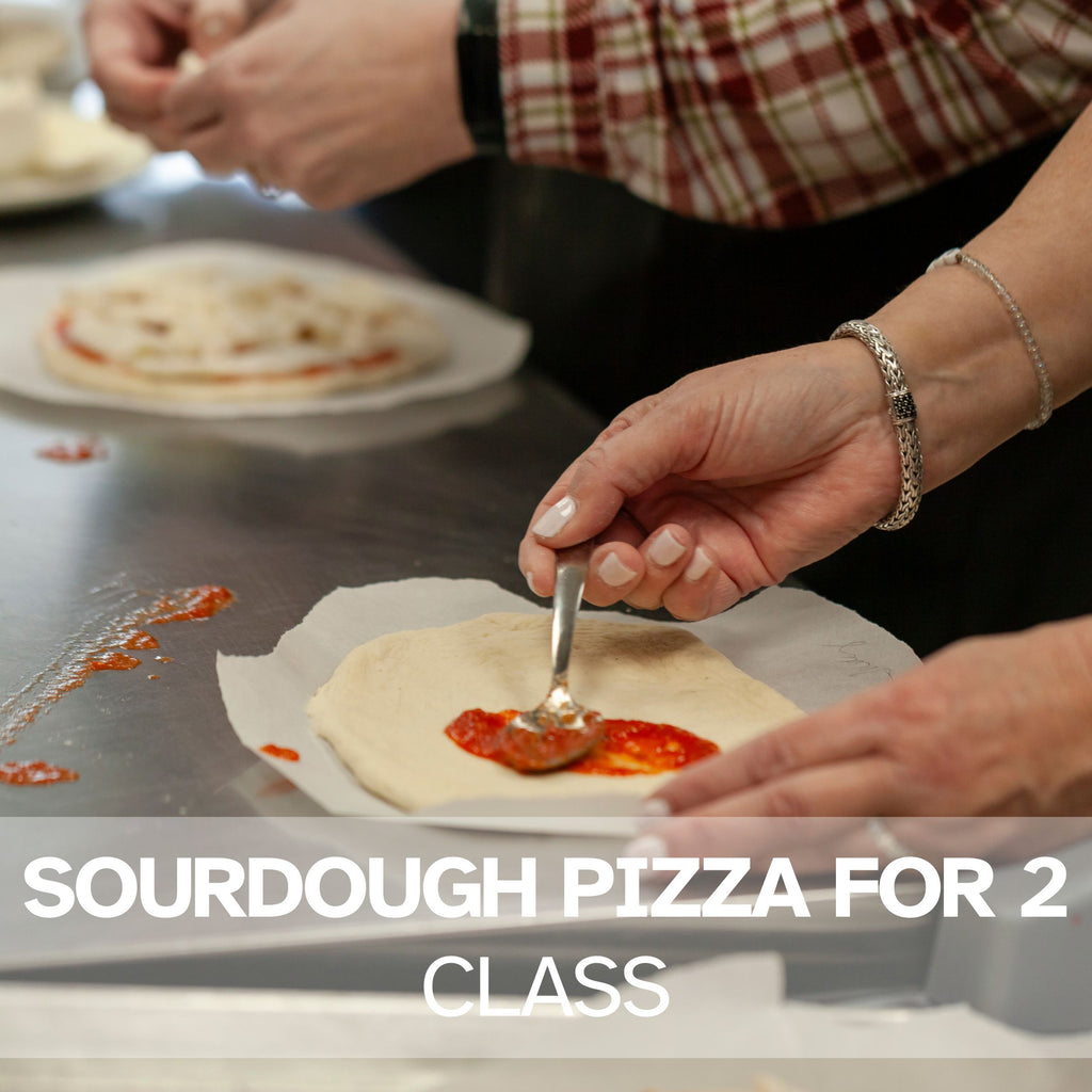 Two people adding toppings to sourdough pizza