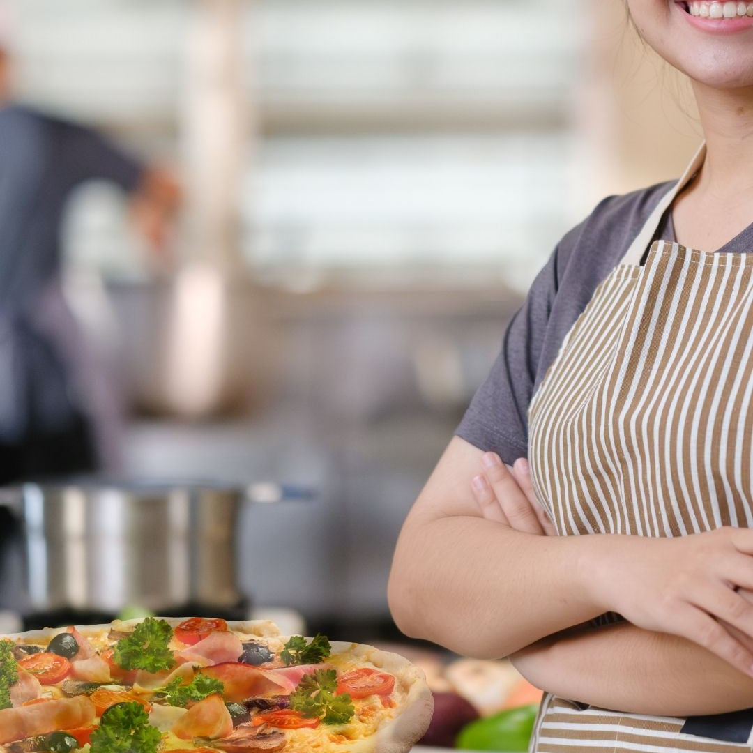 asian teen in commercial kitchen beside pizza
