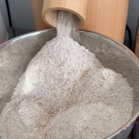 Wooden grinder pouring flour into a metal bowl